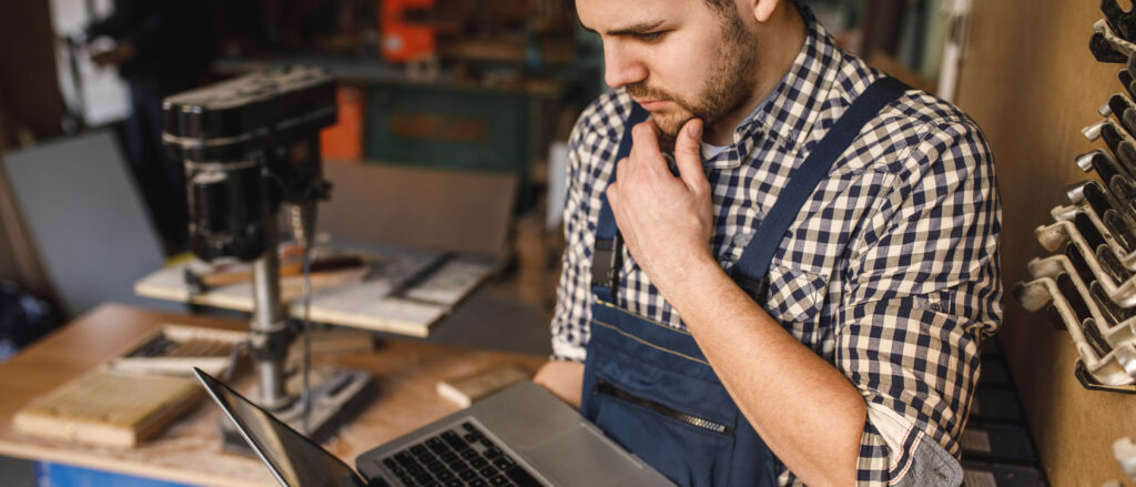 Handwerker in Werkstatt mit Laptop in der Hand,