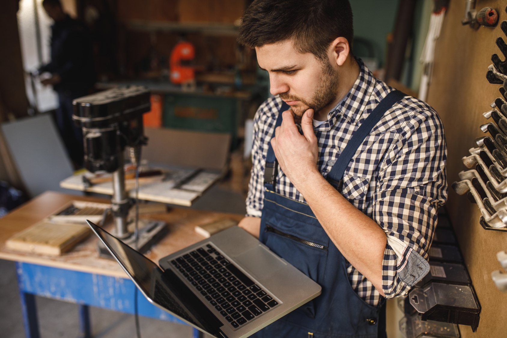 Handwerker in Werkstatt mit Laptop in der Hand.